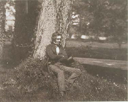 Seated man by the trunk of a tree.
