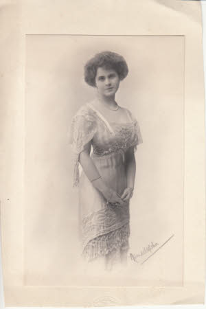 Photograph portrait of Maud Kerr-Smiley as a young woman, standing with hands clasped in front