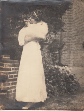Maud Kerr-Smiley standing in a garden wearing a fur stole and holding a small dog