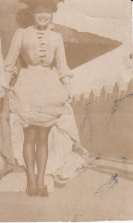 Small photograph, cut from larger photograph, of woman at beach holding dress up to knees