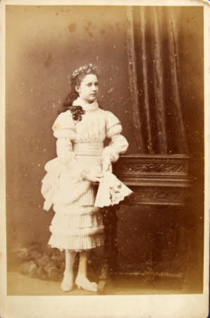 A young lady in a studio setting wearing a pleated dress holding a fan.
