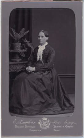 Unknown woman seated in silk dress next to fern.