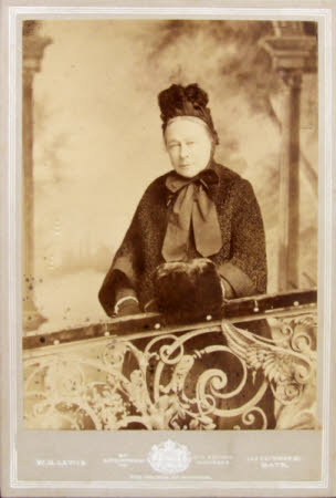 Portrait of an elderly woman wearing a black hat, coat, bow and muff.