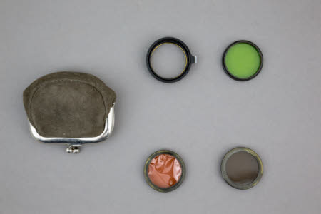 A suede purse containing a filter holder and celluloid filters.