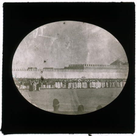 A crowd in front of a long high wall.
